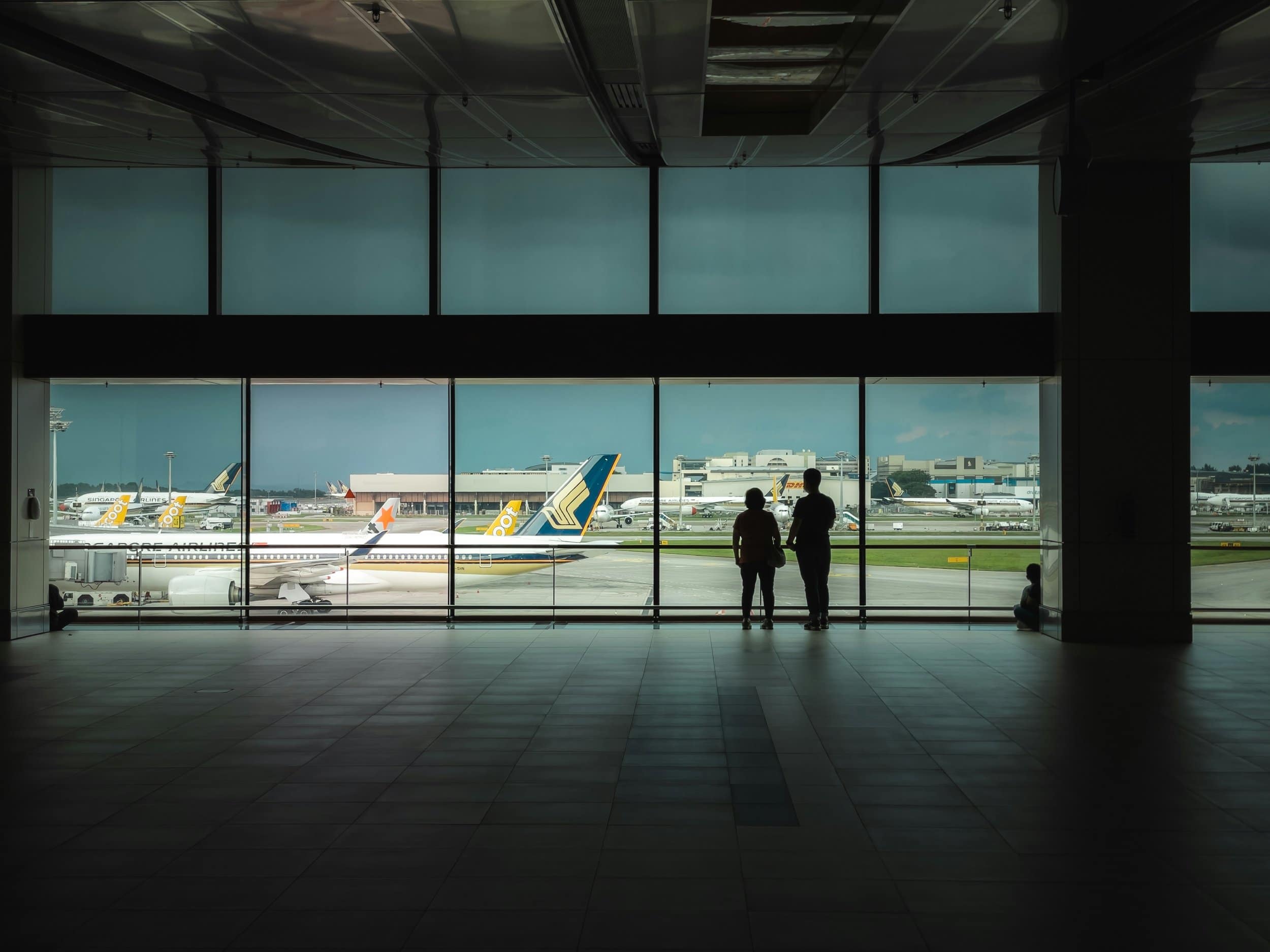 Two people watching aircraft on the apron from an airport terminal window